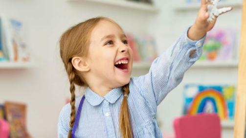 Portrait of adorable little girl enjoying art and craft lesson in development school and smiling happily with hands in paint