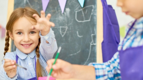 Portrait of adorable little girl  painting pictures enjoying art class in pre school working together with other kids